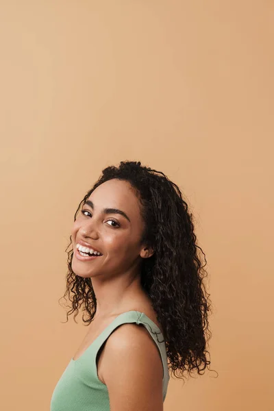 Young black woman with wavy hair laughing and looking at camera isolated over beige background