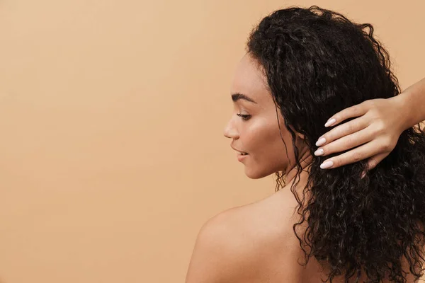 Shirtless black woman with wavy hair posing and looking aside isolated over beige background