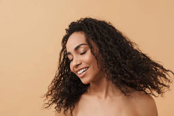 Shirtless black woman with wavy hair laughing at camera isolated over beige background