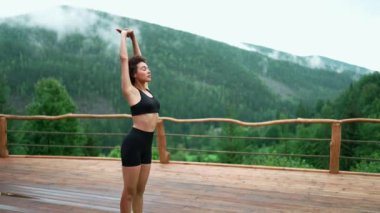 Positive African young sporty woman doing yoga exercise on a yoga mat in the mountains outdoors