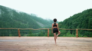 Back view of African young sporty woman doing yoga meditation in the mountains outdoors