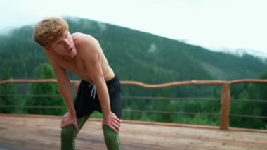 Tired ginger sporty man breathing after sports exercise in the mountains outdoors