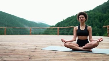 Pretty African young sporty woman doing yoga meditation with closed eyes in the mountains outdoors