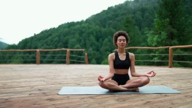 Relaxed African young sporty woman doing yoga meditation with closed eyes in the mountains outdoors