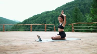 Confident African sporty woman doing meditation with online lesson on laptop in the mountains outdoors
