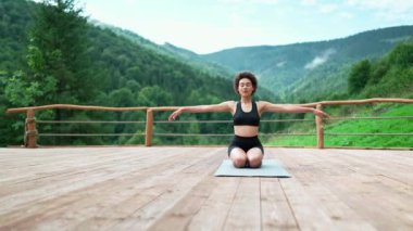 Positive African sporty woman doing breathing exercise with closed eyes in the mountains outdoors