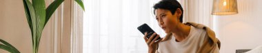 Asian boy talking on mobile phone while sitting on bed at home