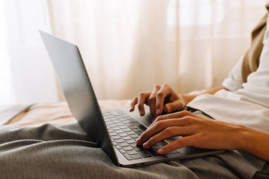 Asian boy working with laptop while resting on bed at home