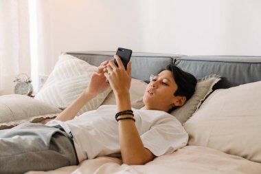 Asian boy using mobile phone while resting on bed at home