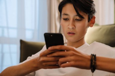 Asian boy using mobile phone while sitting on floor at home