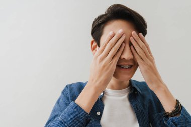 Asian boy wearing shirt covering his eyes while posing on camera isolated over white background