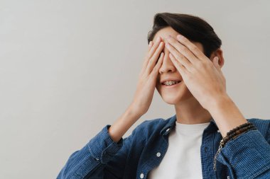 Asian boy wearing shirt covering his eyes while posing on camera isolated over white background