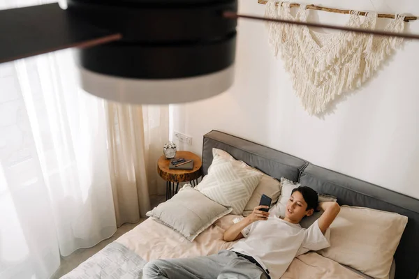 Asian Boy Smiling Using Mobile Phone While Resting Bed Home — Stok Foto
