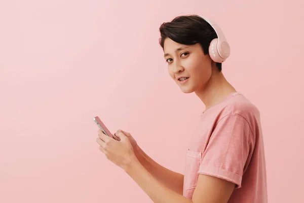 Asian Boy Listening Music Headphones Using Mobile Phone Isolated Pink — Stockfoto