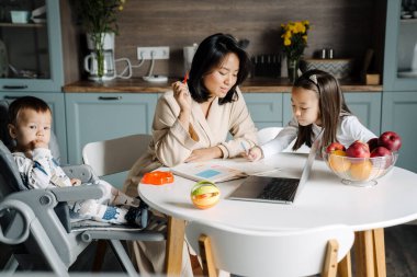 Genç anne, annesiyle mutfakta ödev yapıyor.