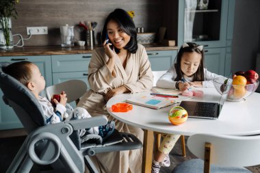 Mutlu anne çocuklarıyla evde vakit geçirirken cep telefonuyla konuşuyor.