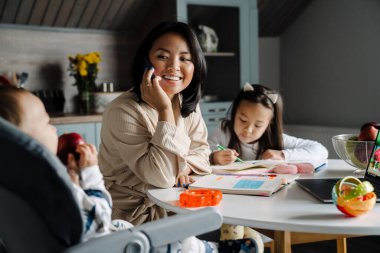 Mutlu anne çocuklarıyla evde vakit geçirirken cep telefonuyla konuşuyor.