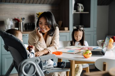 Mutlu anne çocuklarıyla evde vakit geçirirken cep telefonuyla konuşuyor.