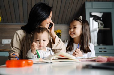 Mutlu anne çocuklarıyla evde vakit geçirirken cep telefonuyla konuşuyor.