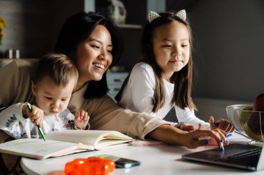 Mutlu anne çocuklarıyla evde vakit geçirirken dizüstü bilgisayar kullanıyor.