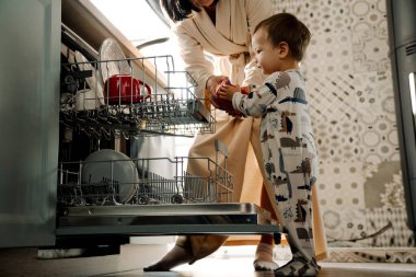 Oğluyla evde ev işi yaparken bulaşık makinesini kullanan mutlu bir anne.