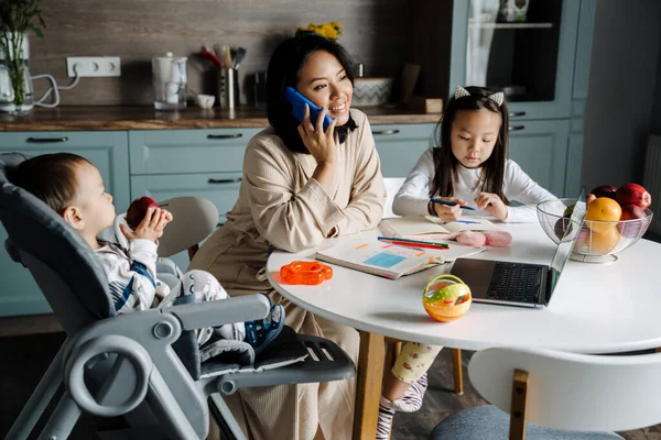 Mutlu anne çocuklarıyla evde vakit geçirirken cep telefonuyla konuşuyor.