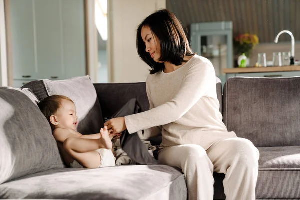 亚洲的年轻女子坐在家里的沙发上 穿着她的儿子 — 图库照片