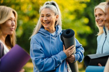 Yaz parkında yoga yaptıktan sonra konuşan ve gülümseyen çok ırklı kadınlar.