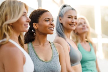 Yoga antrenmanından sonra duvar kenarında konuşan ve gülen çok ırklı kadınlar.