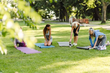 Çok ırklı kadınlar yaz parkında yoga yaparken minderlerini açıyorlar.