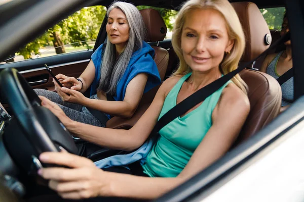 Mujeres Multiraciales Sonriendo Utilizando Teléfono Celular Mientras Conduce Coche Día —  Fotos de Stock