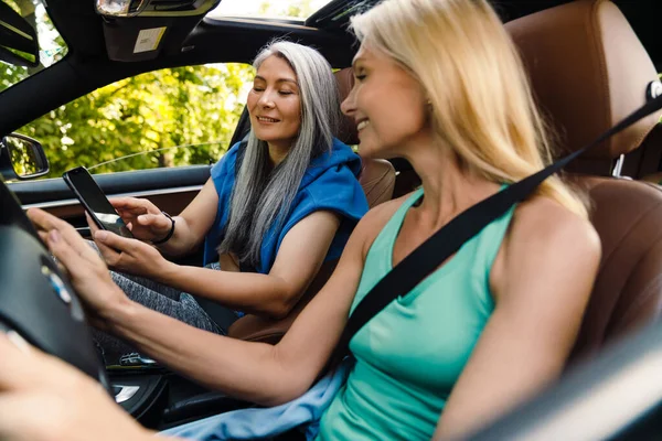 Mujeres Multiraciales Sonriendo Utilizando Teléfono Celular Mientras Conduce Coche Día —  Fotos de Stock