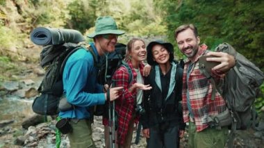 Neşeli çok ırklı turist arkadaşları açık havada dağlarda cep telefonlarında selfie çekiyorlar.