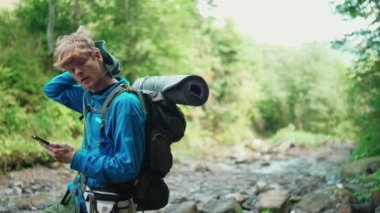 Ciddi kızıl saçlı turist dağlarda nehir kenarında cep telefonuyla yazı yazıyor.