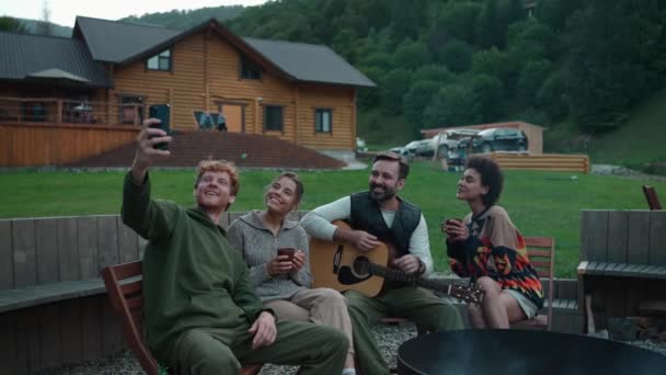Neşeli Çok Uluslu Arkadaşlar Dağlarda Ateşin Etrafında Otururken Telefonda Gitar — Stok video