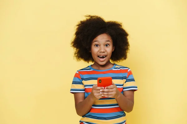 在黄色背景下使用隔离手机表达惊讶的年轻黑人女孩 — 图库照片