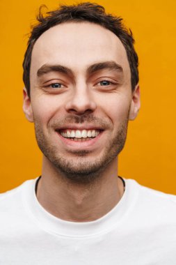 Turuncu arka planda izole bir şekilde duran gülümseyen genç bir adamın portresini yakından çek.