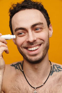 Mutlu orta yaşlı beyaz adam yüzüne nemlendirici krem sürüyor turuncu arka planda.