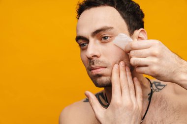 Sarı duvarda yüzüne masaj yapmak için kuvars taşı kullanan orta yaşlı esmer bir adamın portresini kapat.