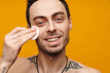 Sarı duvarın üzerinde pamuk kullanan, orta yaşlı, gülümseyen bir adamın portresini yakından çek.