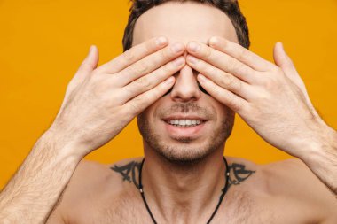 Gülümseyen üstsüz esmer adam, sarı arka planda izole edilmiş gözleri örtüyor.