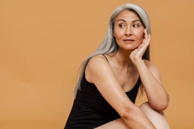 Olgun Asyalı güzel bir kadın, sarı arka planda izole edilmiş, gülümseyen ve kameraya poz veren.