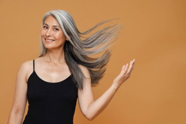 Olgun Asyalı güzel bir kadın, sarı arka planda izole edilmiş, gülümseyen ve kameraya poz veren.