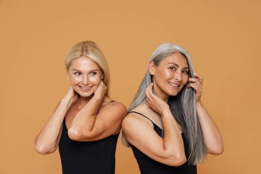 Olgun, çok ırklı, güzel kadınlar eşofman giyiyor, gülümsüyor ve sarı arka planda soyutlanmış poz veriyorlar.