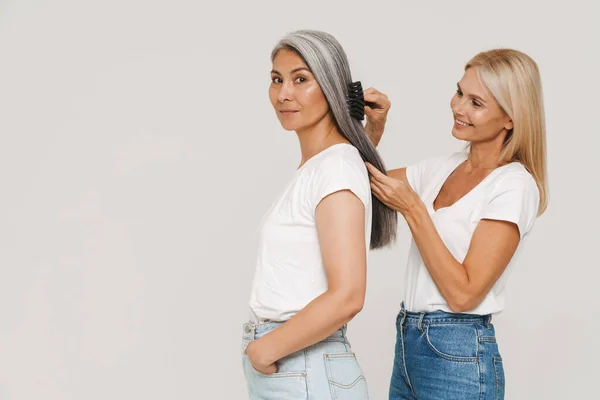 Mature Multiracial Women Wearing Shirts Smiling Brushing Hair Together Isolated — Stock Photo, Image