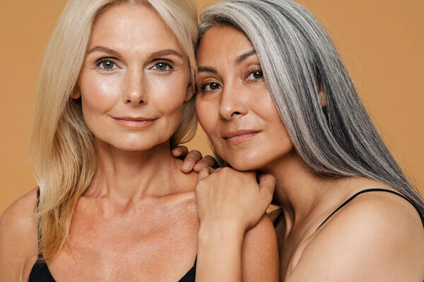 Зрелые многорасовые красивые женщины в телесных костюмах улыбаются и позируют изолированно на желтом фоне