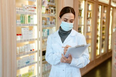 Eczanede çalışan laboratuvar önlüğü ve yüz maskesi giyen beyaz eczacı.