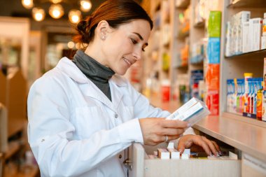 Eczanede çalışırken gülümseyen laboratuvar önlüğü giyen beyaz eczacı.