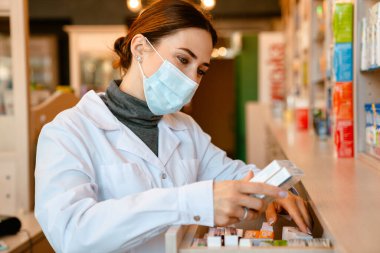 Eczanede çalışan laboratuvar önlüğü ve yüz maskesi giyen beyaz eczacı.