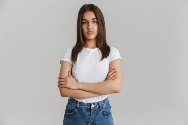 Gri duvar arkası kolları katlanmış, uzun esmer saçlı, rahat olmayan beyaz bir kadının portresi.